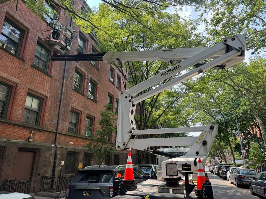 Skyway truck-mounted lift cleaning the windows of a brick apartment building on a tree-lined street