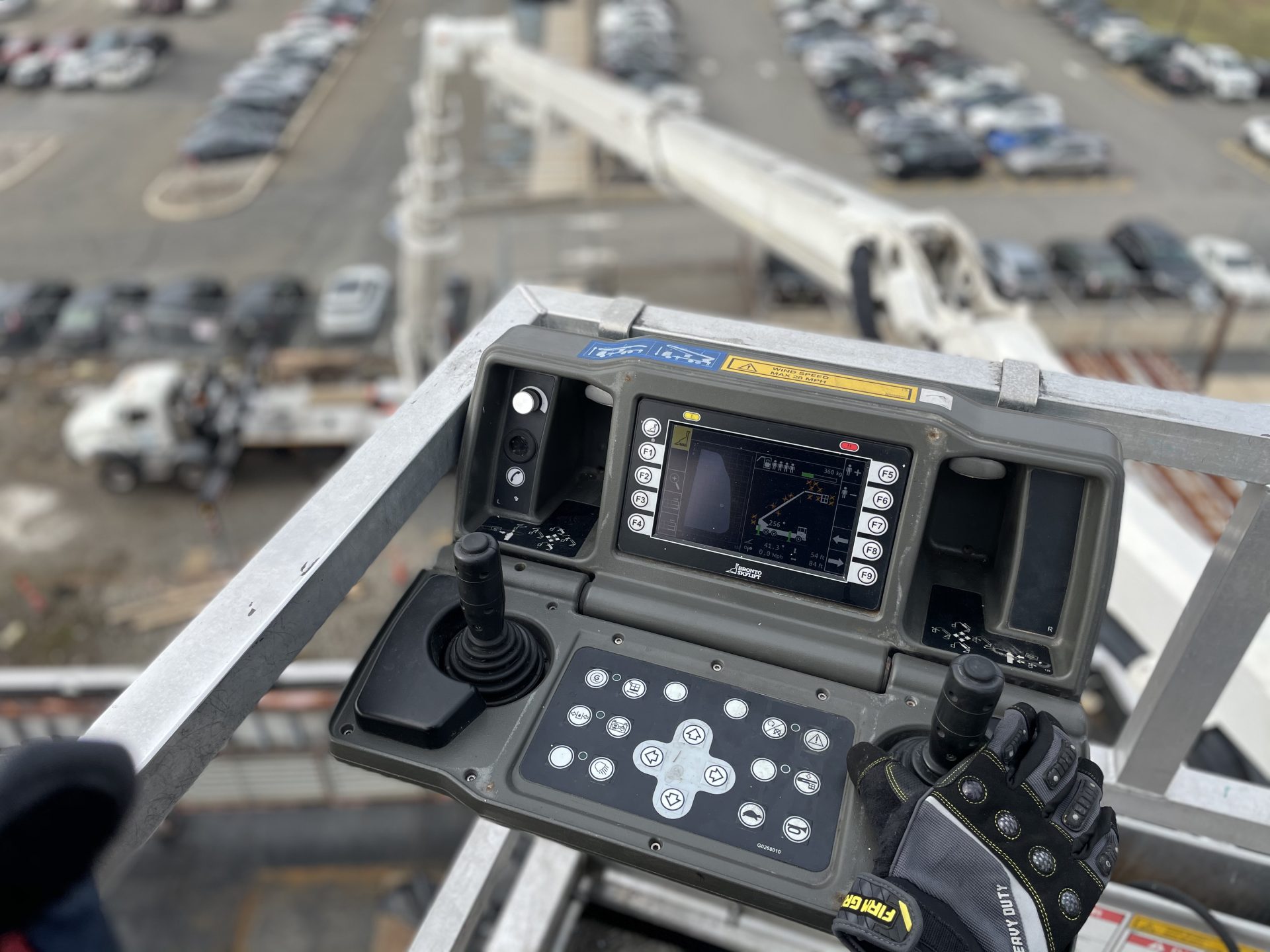 Gloved operator hand on the Skylift basket control panel, with the lift boom and truck far below