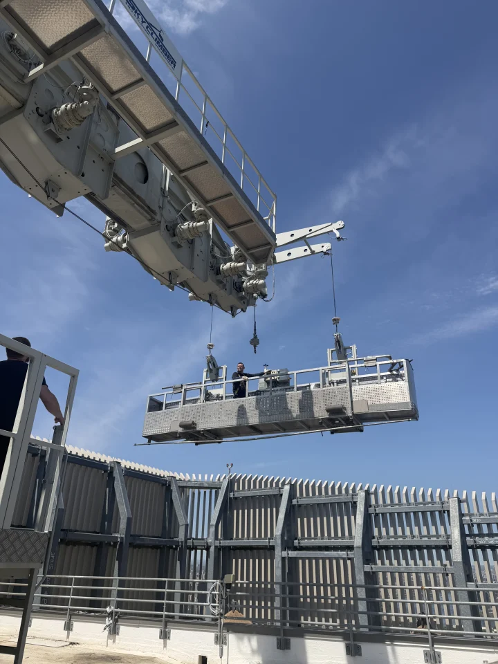 Window cleaning gondola lowered from a rooftop building maintenance unit