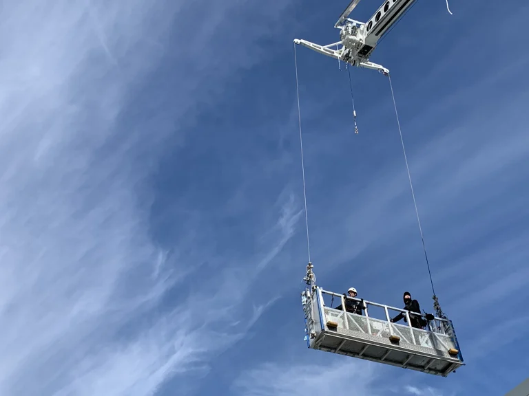 Window cleaning gondola with two technicians suspended from a roof