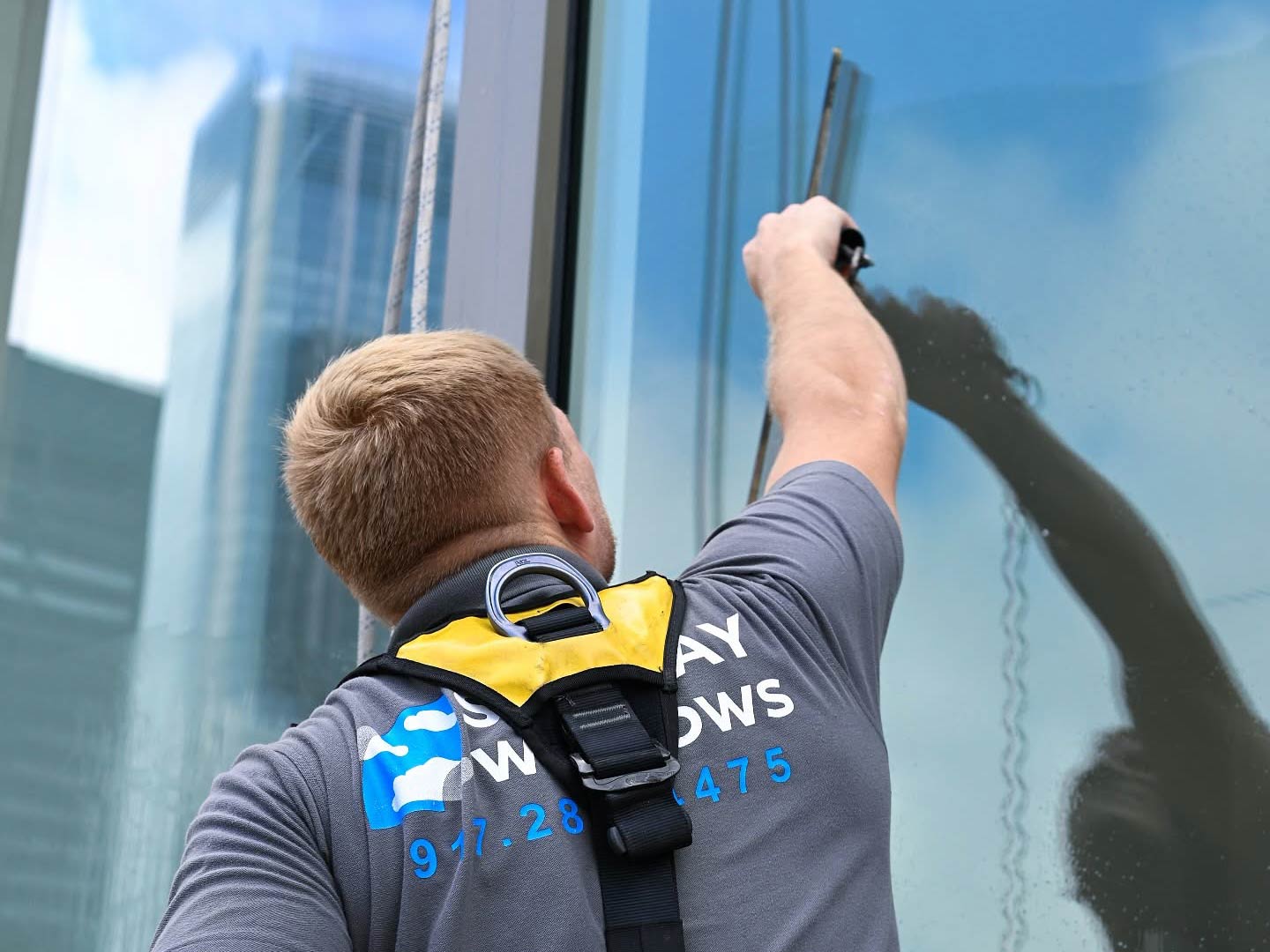 Skyway technician in a harness squeegeeing a large glass window