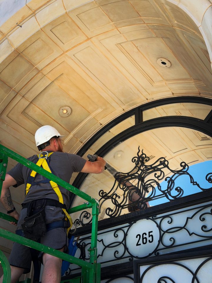 Skyway technician in a helmet and harness cleaning the ironwork and glass above a townhouse entrance