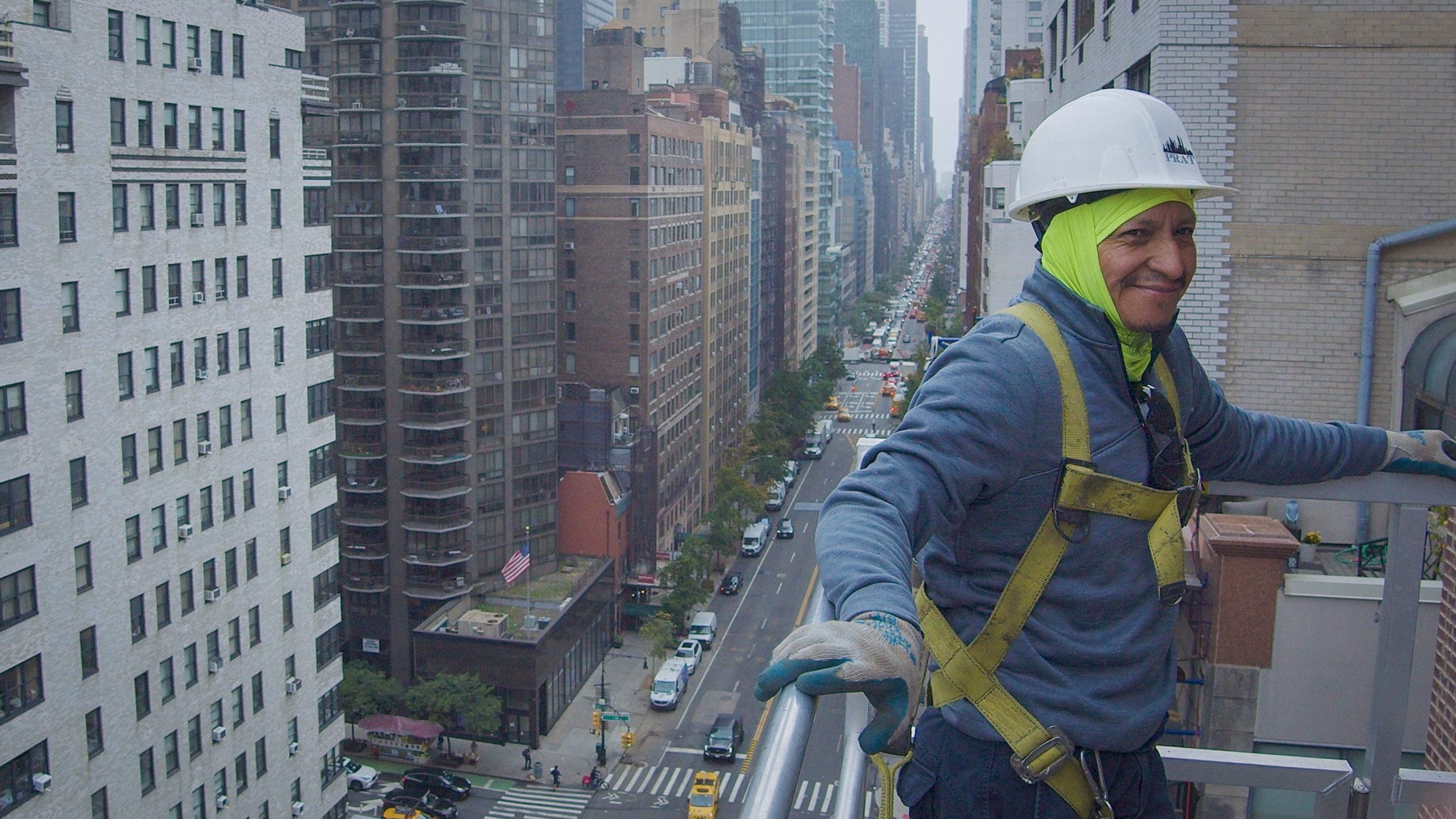 Skyway lift operator wearing a hard hat and safety harness in the aerial lift basket high above a Manhattan avenue