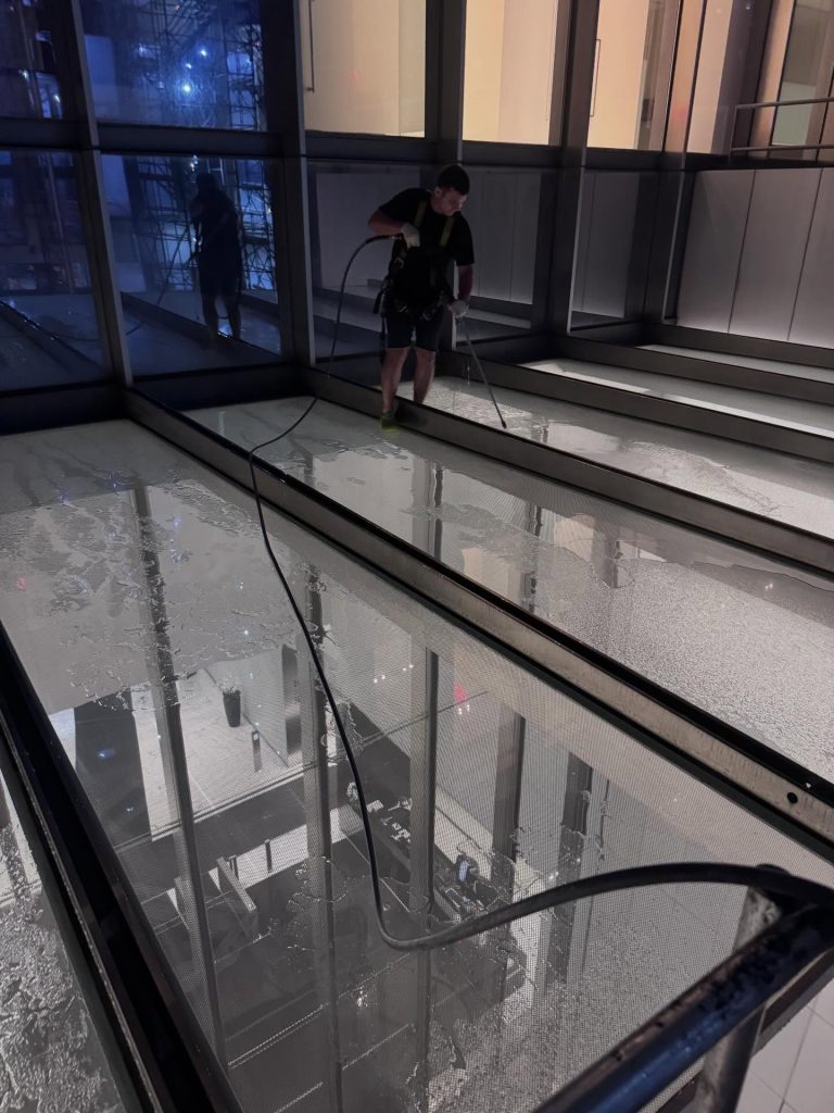 Skyway technician cleaning glass floor panels in a newly finished building