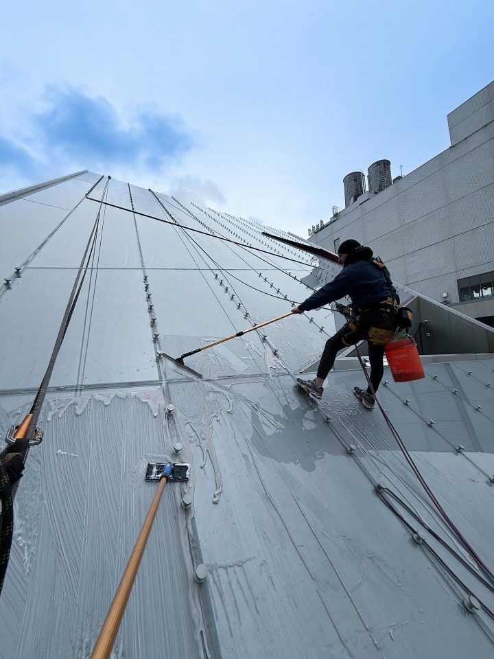 Two Skyway rope access technicians cleaning a sloped glass skylight roof