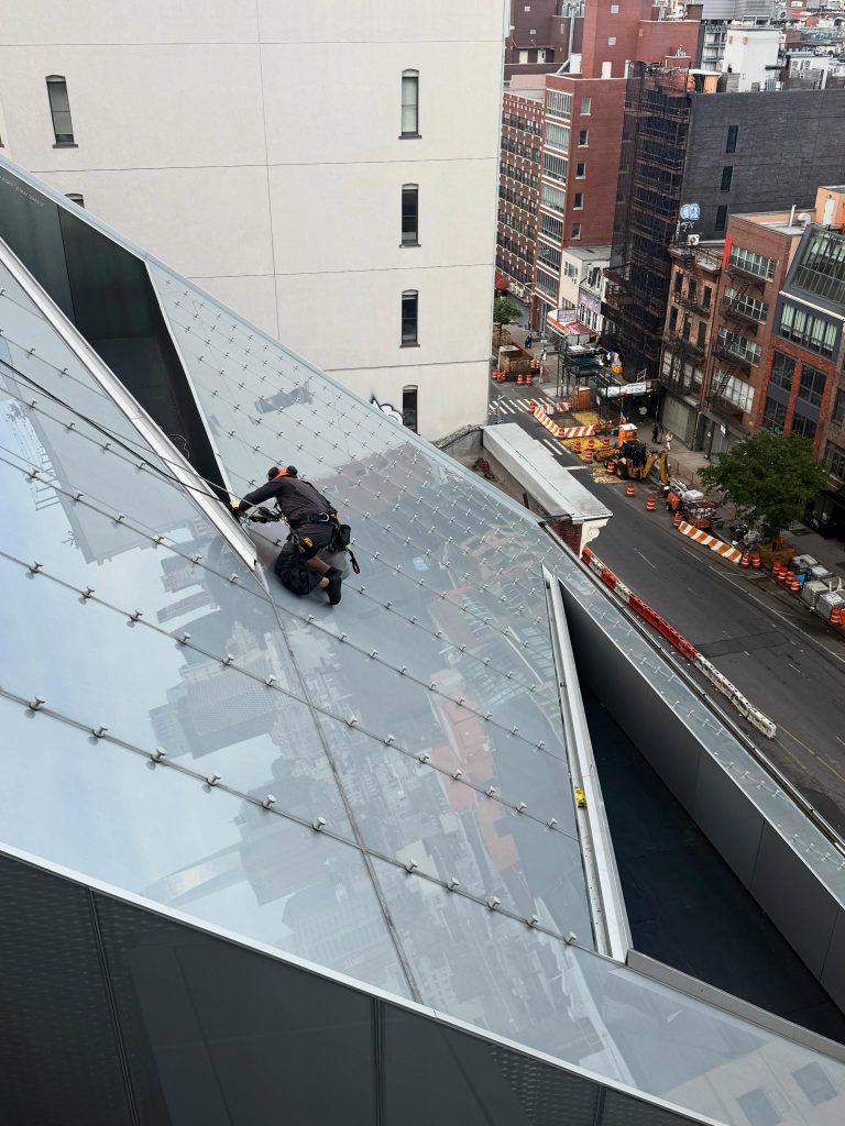 Rope access technician cleaning an angled glass skylight above a New York street