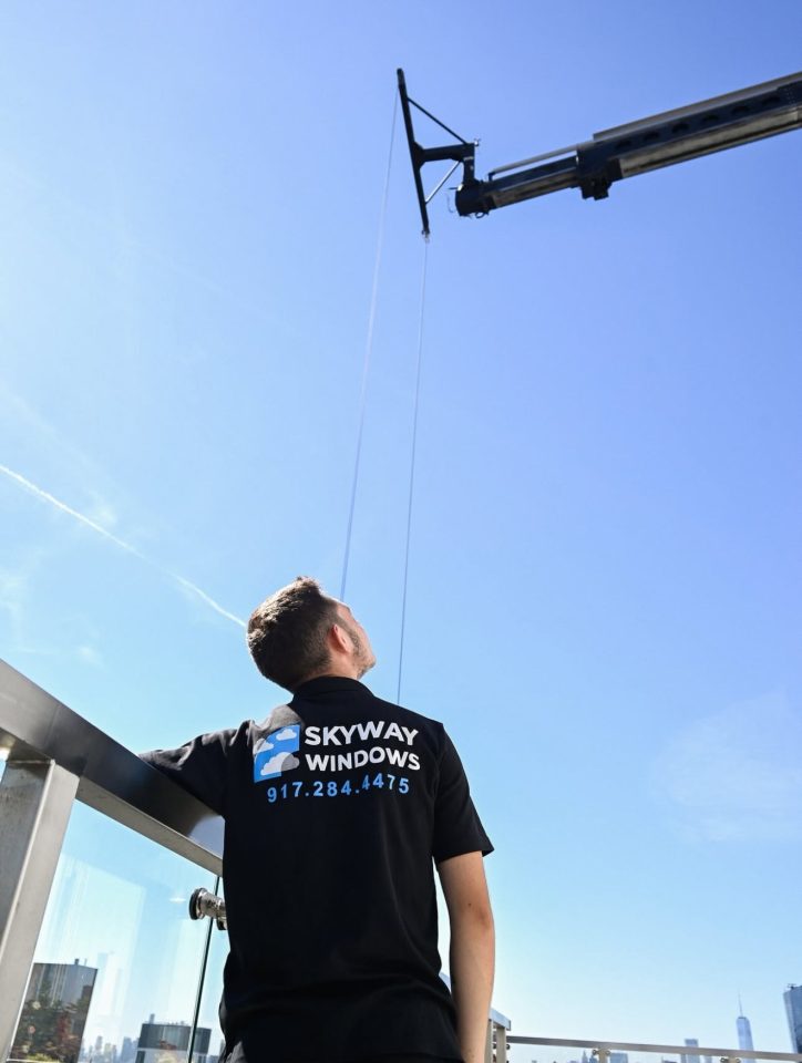 Skyway Windows technician on a rooftop terrace looking up at the boom of a truck-mounted aerial lift