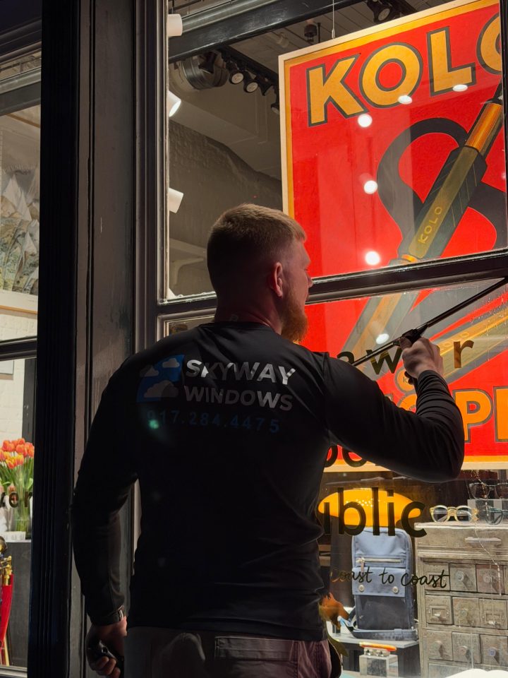 Skyway technician squeegeeing a storefront window with a bright red display