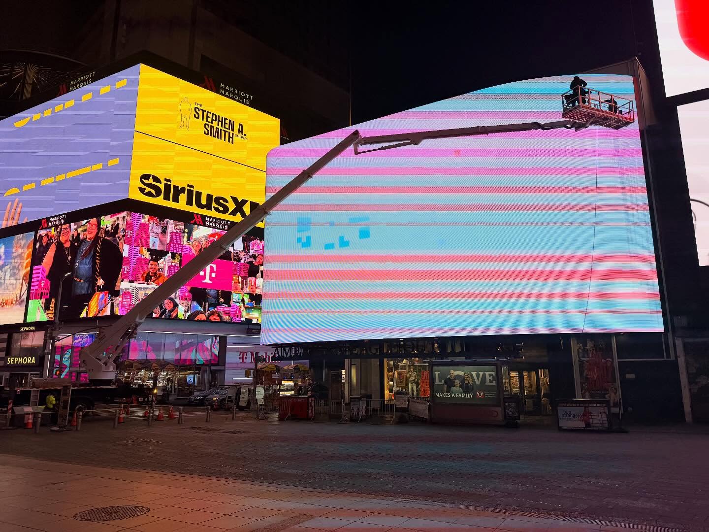 Skyway truck-mounted lift beside a giant LED screen in Times Square at night